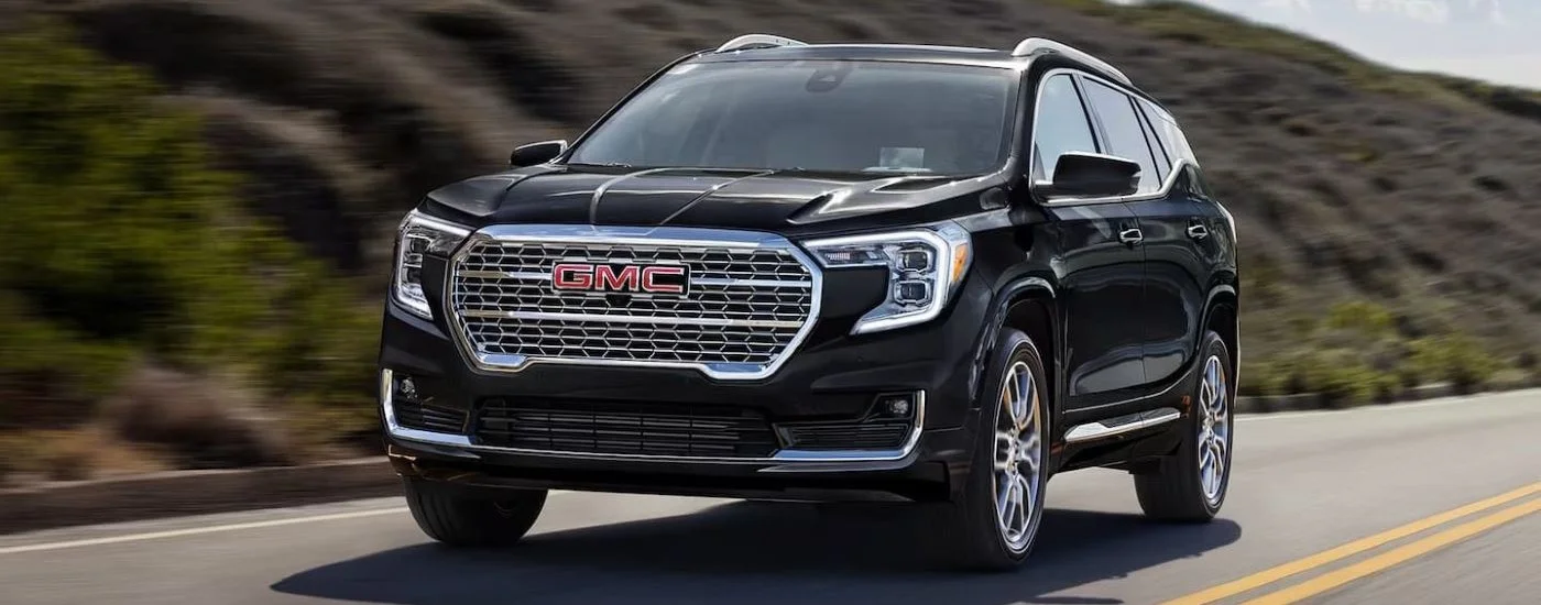 A black 2024 GMC Terrain Denali driving by a grassy hill.
