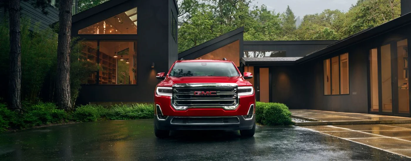 A red 2023 GMC Acadia parked outside a modern house.