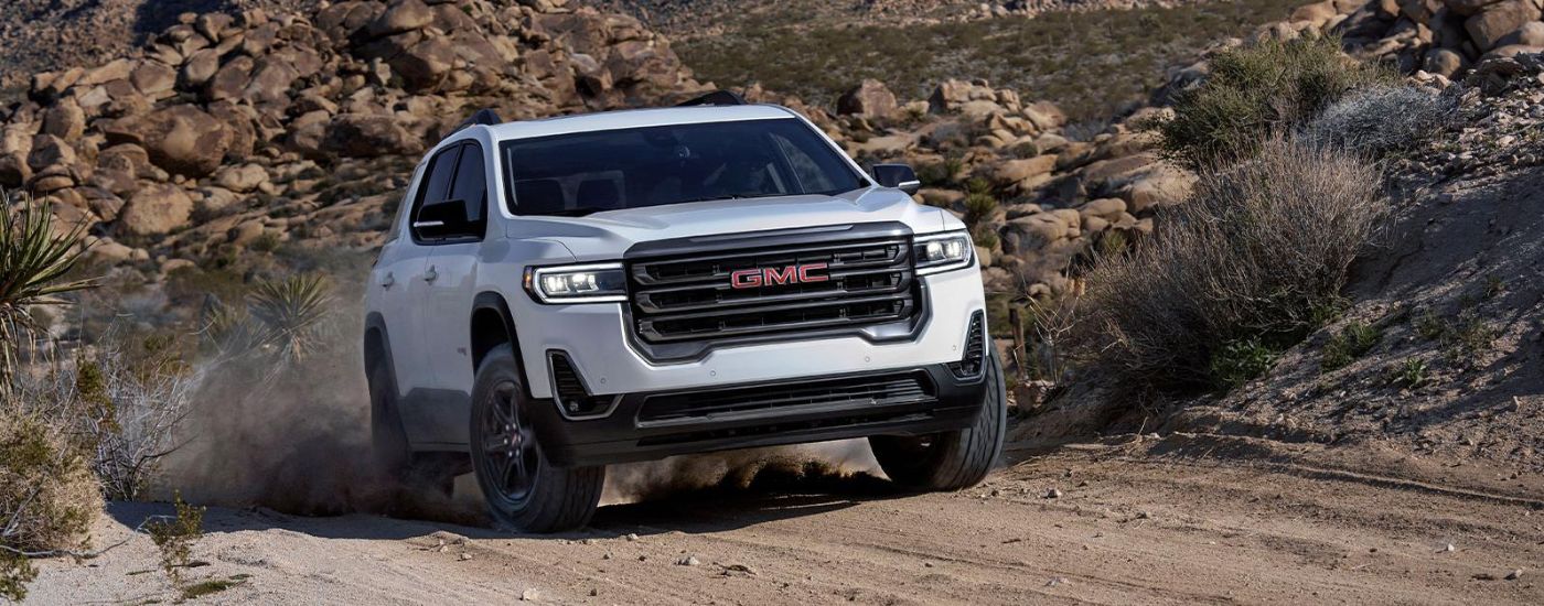 White 2022 GMC Acadia driving off-road on a dirt road.