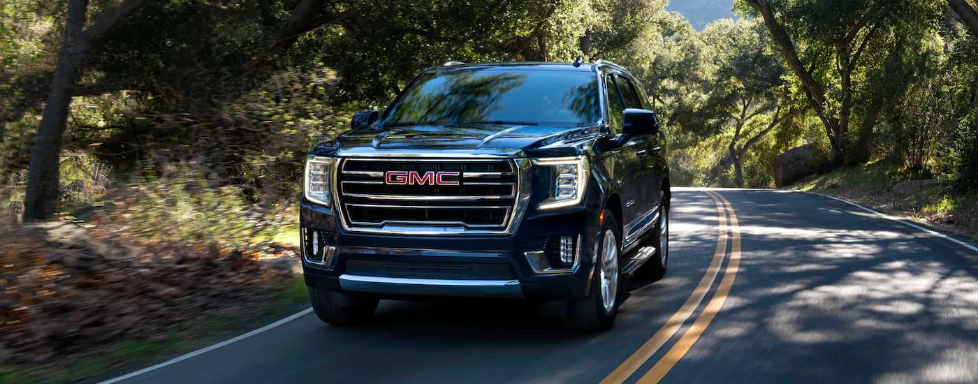 Black 2023 GMC Yukon driving on a forested road