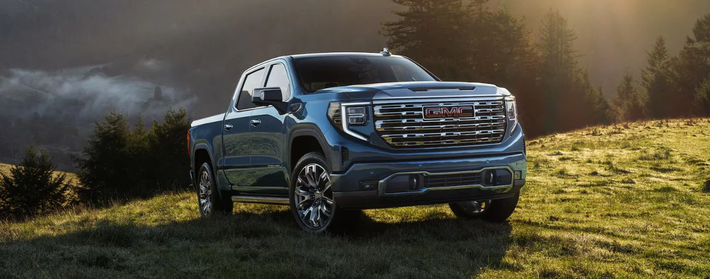 Blue 2026 GMC Sierra 1500 parked in the grass at sunrise.