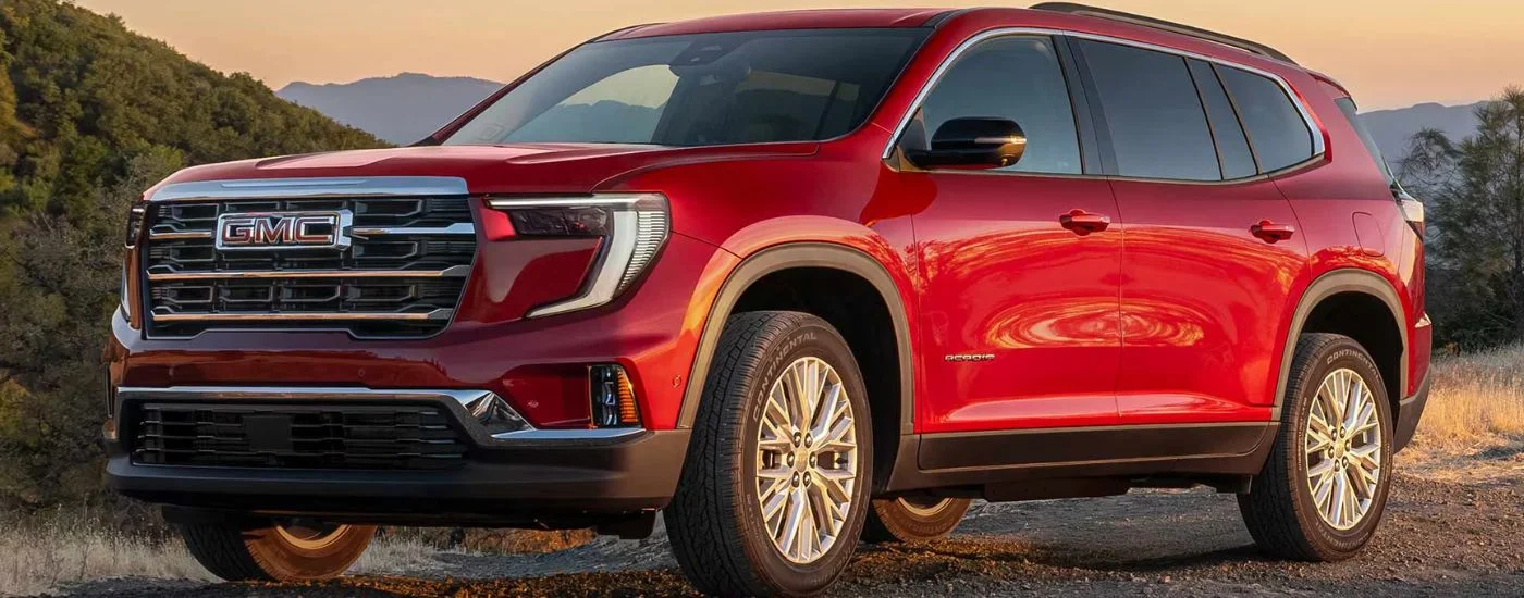 Red 2026 GMC Acadia parked on a dirt trail.