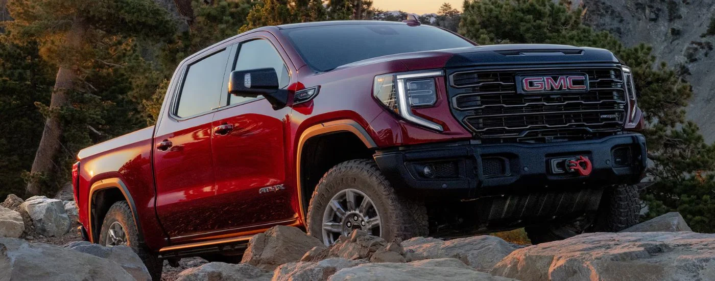 Red 2026 GMC Sierra 1500 driving up rough terrain.