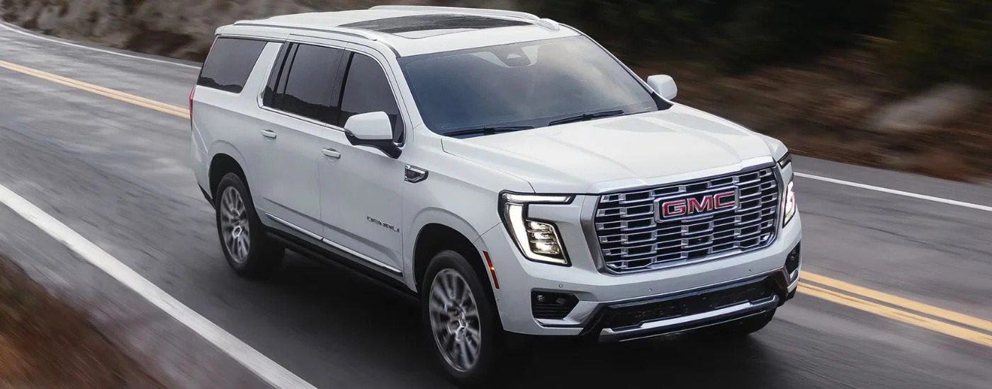 White 2026 GMC Yukon Denali aerial view driving on a paved road.