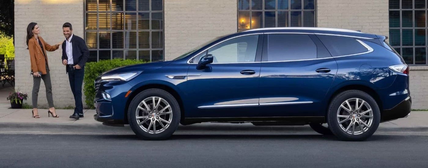 A blue 2023 Buick Enclave parked by people.