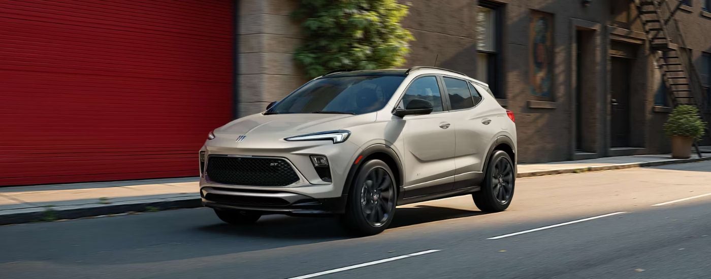 A silver 2026 Buick Encore GX shown driving by a building.